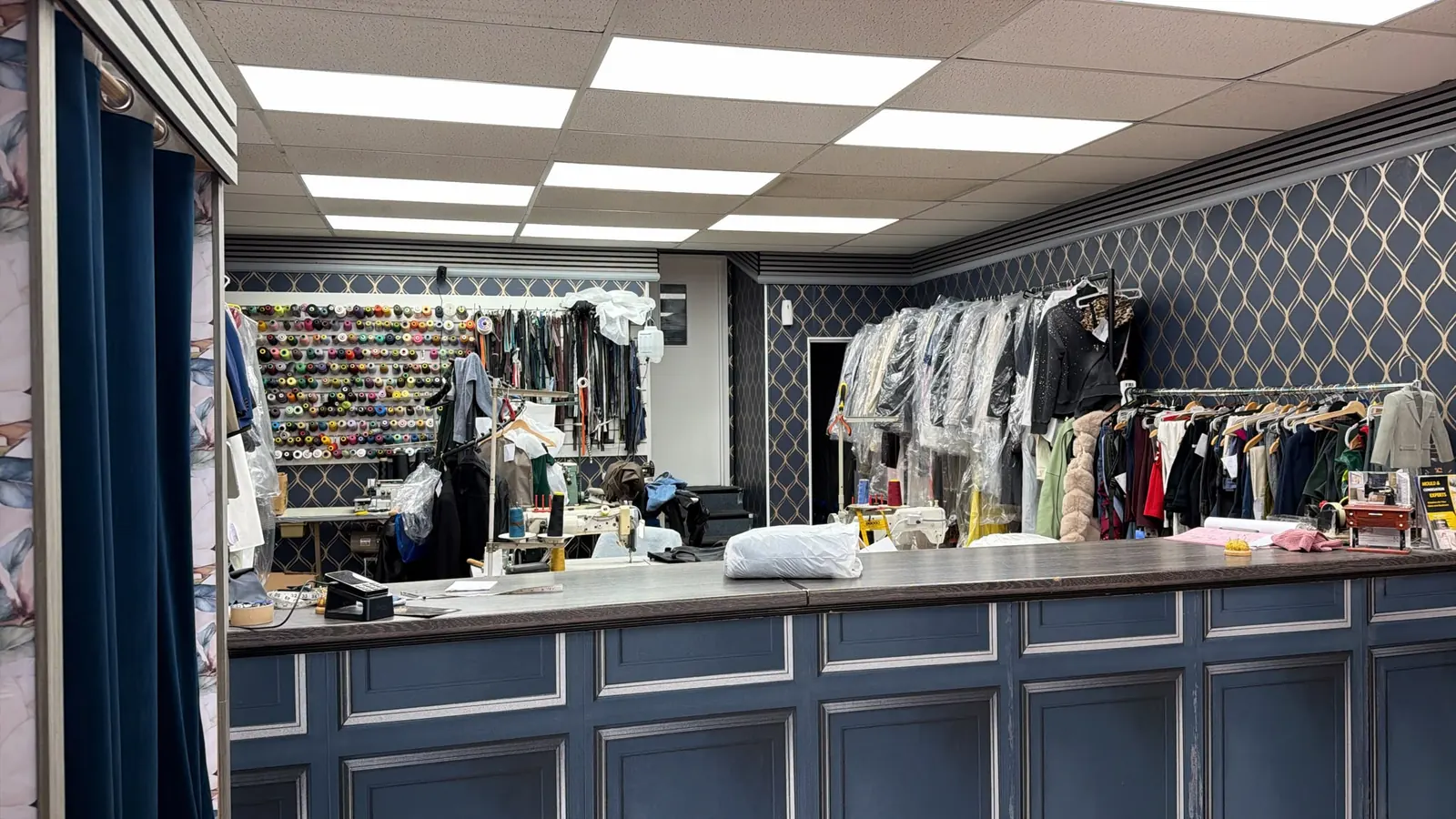 Inside Best Stitch: a navy panelled counter, a wall of thread reels and rails of garments waiting for collection